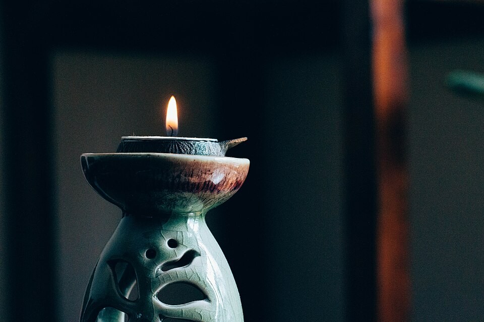 A small flame burning in a ceramic holder against a dark background